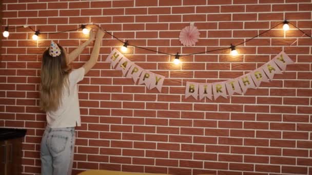 A menina decora o quarto para o feriado com guirlandas e bandeiras, traseira — Vídeo de Stock