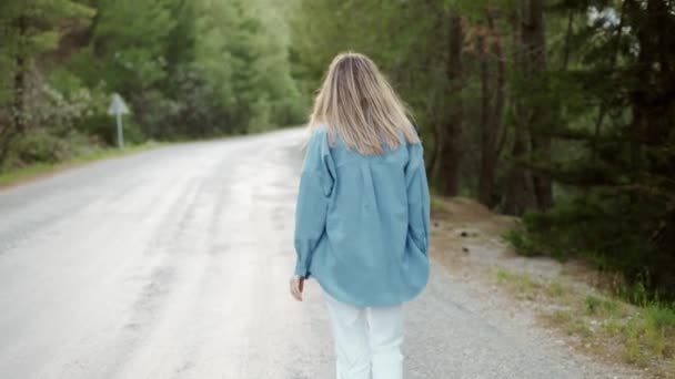 Vrouw loopt op verharde weg in het bos, achteraanzicht — Stockvideo