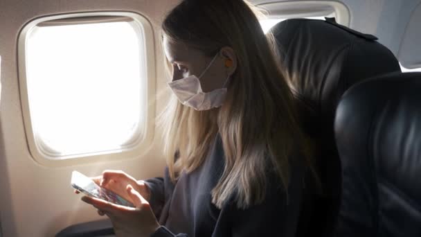 Женщина использует защитную маску, играя со своим телефоном в самолете — стоковое видео
