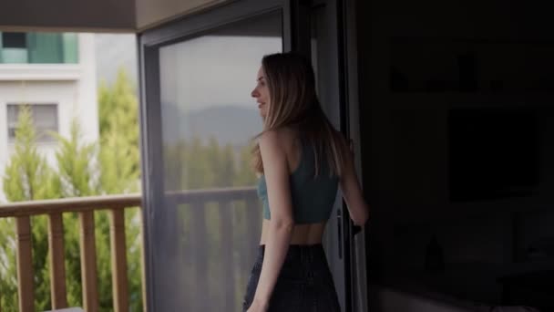En blondin står nära ett träräcke på verandan, beundrar utsikten — Stockvideo