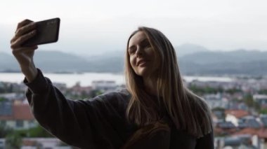 Uzun saçlı kadın elinde akıllı telefonuyla fotoğraf çekiyor.
