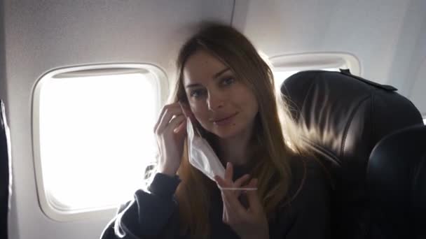 Blondynka zakładająca maskę w samolocie i uśmiechnięta — Wideo stockowe