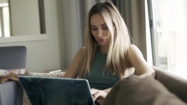 Geconcentreerde vrouw zittend op sofa browsen sociale media op laptop — Stockvideo
