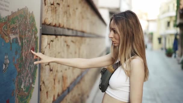 Blondynka turystka stojąca przy ścianie, wskazująca palcem — Wideo stockowe