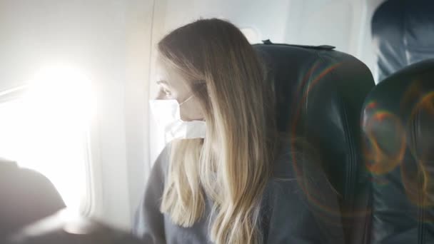 Женщина в защитной маске на самолете смотрит в окно — стоковое видео