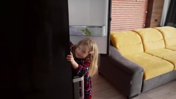 Cute little girl otwiera drzwi lodówki sięgając po coś — Wideo stockowe