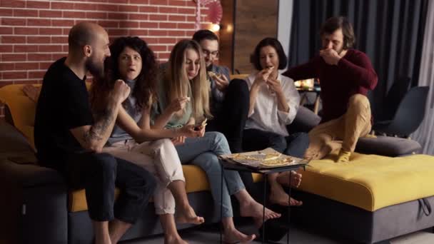 Nära vänner sitter i soffan - chatta, äta pizza, le — Stockvideo