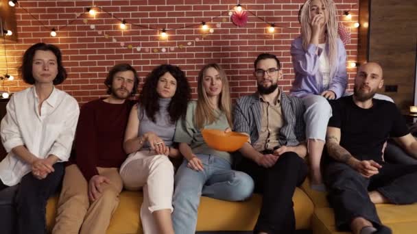 Portret van vrienden kijken comedy show op TV en eten popcorn terwijl zitten op een bank thuis — Stockvideo