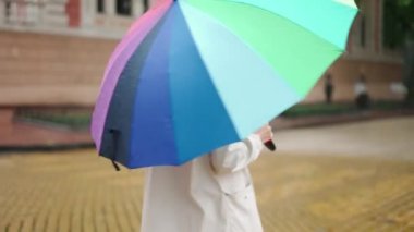 Yağmurun altında yürüyen çok renkli şemsiyeli bir kadın.