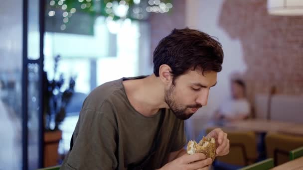 Unshaven c uomo mangia hamburger di carne con piacere, morde hamburger con la bocca — Video Stock