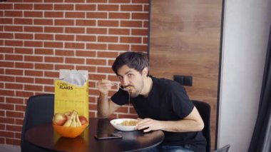 Mısır gevreği yiyen adam, kamera önünde komik poz veriyor.