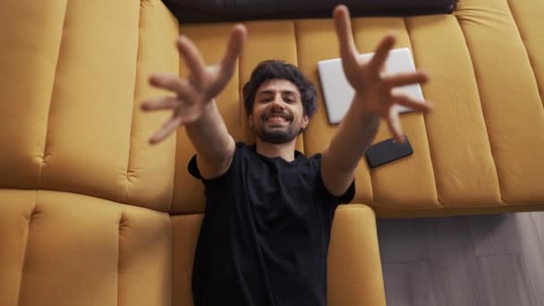 Top view of a young man lying on couch at home stretching hands to the camera — Stock Video