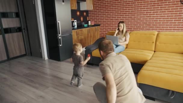Far leker med sitt barn hemma medan deras mamma är upptagen med sin laptop i soffan — Stockvideo