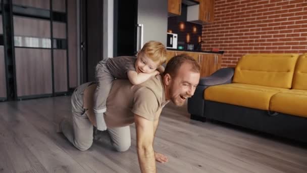 Apa játszik a fiával, háton lovagolja a nappaliban. — Stock videók