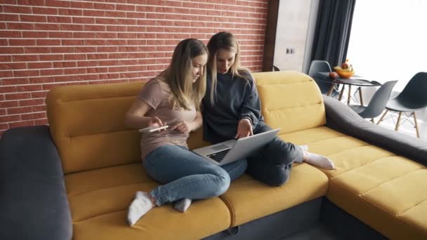 Δύο χαρούμενοι φίλοι βλέποντας περιεχόμενο πολυμέσων σε ένα φορητό υπολογιστή που κάθεται σε έναν καναπέ — Αρχείο Βίντεο