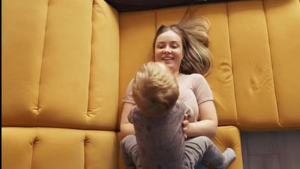 Женщина качается и воспитывает ребенка, лежа на диване, вид сверху — стоковое видео