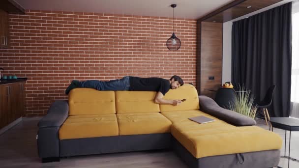 Ein Mann legt sich auf Sofas und blickt auf ein Handy — Stockvideo