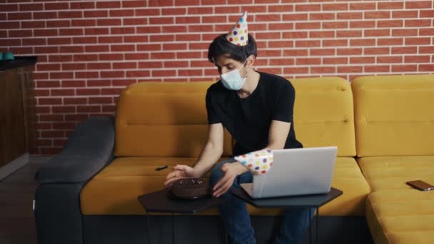 Человек в маске, одинокий парень закрывает ноутбук после празднования дня рождения — стоковое видео