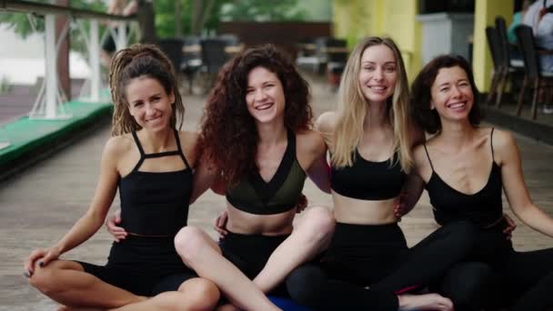 Fröhliche junge Mädchen in Sportbekleidung sitzen in einer Umarmung auf dem Boden, nachdem sie Yoga praktiziert haben — Stockvideo