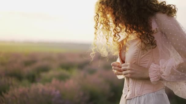 Curly-haired girl in a pink dress, tight her corset among a purple lavender field — Stock Video