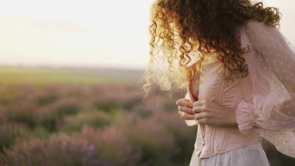 Chica de pelo rizado en un vestido rosa, apretado su corsé entre un campo de lavanda púrpura — Vídeo de stock