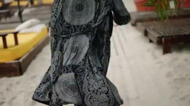 Bir yaz günü kumsalda koşan, çıplak ayaklı, zarif bir peignoir giymiş bir kadının arkası.