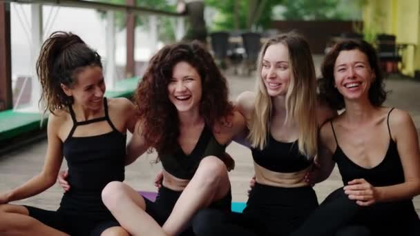 Ragazze sorridenti in abbigliamento sportivo sedersi in un abbraccio sul pavimento, dopo aver praticato yoga — Video Stock