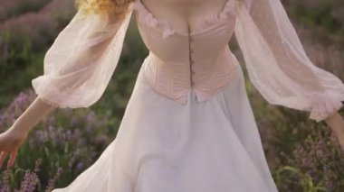 Pembe elbiseli kadın lavanta tarlasında neşeyle koşuyor ve çiçeklere dokunuyor.