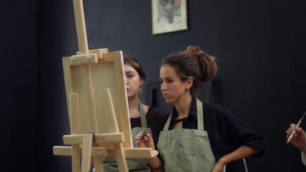 Estudiante y profesor de arte durante la lección de pintura de pie frente al caballete — Vídeo de stock