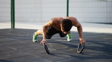 Güçlü, kaslı adam halkalarla şınav çekiyor.