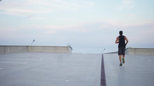 El hombre corre al aire libre en el garaje del nivel de estacionamiento con los brazos extendidos — Vídeos de Stock