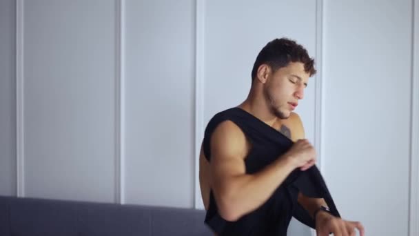 Handsome young man with bare torso is putting on a t-shirt at home — Stock Video