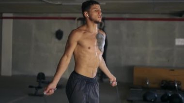 Çıplak gövdeli kaslı adam atlamak için ip kullanıyor.