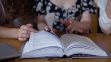 Kütüphanede birlikte kitap okuyan üç öğrenci, metne işaret ediyor.