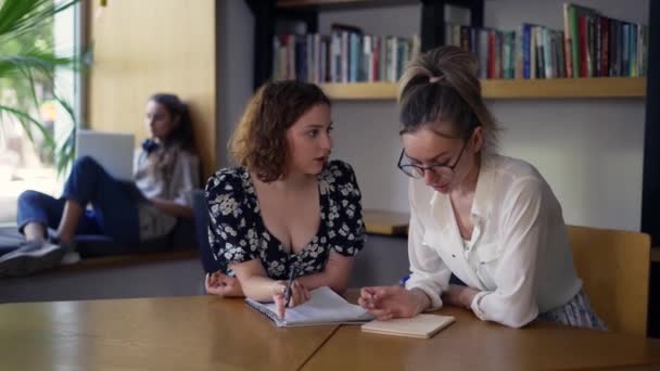 Dua siswa perempuan dewasa mendiskusikan proyek baru di perpustakaan — Stok Video