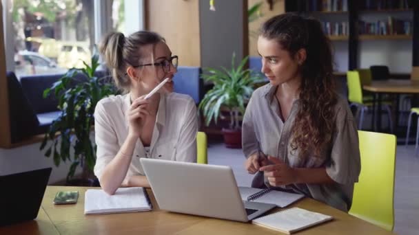 Två kvinnliga studenter diskuterar nytt projekt i biblioteket — Stockvideo