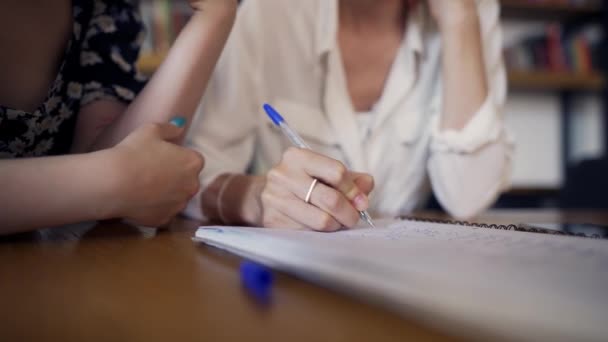 Dos chicas están sentadas en la mesa y escribiendo notea en un cuaderno — Vídeo de stock