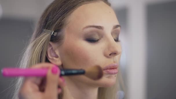 化粧作家は若いブロンドの顔の表面に粉を適用します。 — ストック動画