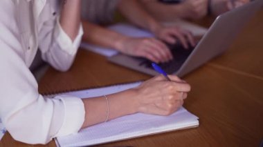 Üç yetişkin öğrenci yeni projeyi tartışıyor, notlar alıyorlar.