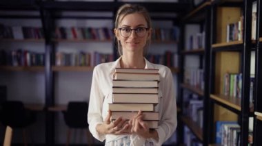 Kütüphanede bir sürü kitap tutan ve gülümseyen bir kadının portresi.