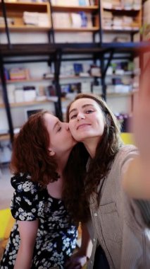 İki komik kız kütüphanede telefonda selfie çekiyor, pilice öpücük yolluyor.