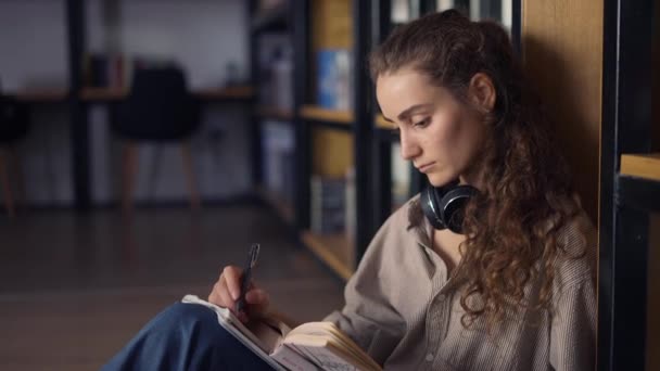 Étudiant s assis contre bibliothèque écrire des notes dans le bloc-notes — Video