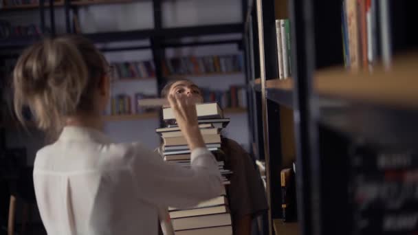 Kız öğrenci kütüphanede bir sürü kitap tutuyor, arkadaşı daha da fazla... — Stok video