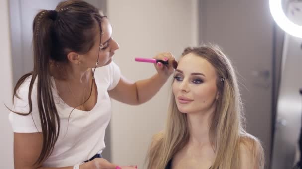 Make-up umělec aplikuje prášek k dokončení klientské make-up v jasném studiu — Stock video