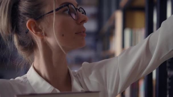 Mujer sexy sosteniendo pila de libros en la biblioteca, poniendo más en la pila — Vídeos de Stock