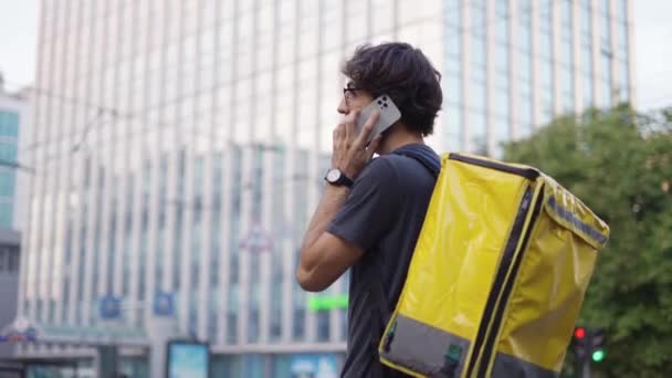 Livreur avec sac à dos appelant un client dans la rue de la ville — Video