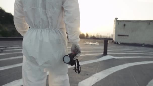 보호용 양복을 입고마스크와 인공호흡기를 손에 들고 걷고 있는 알아볼 수없는 근로자 — 비디오