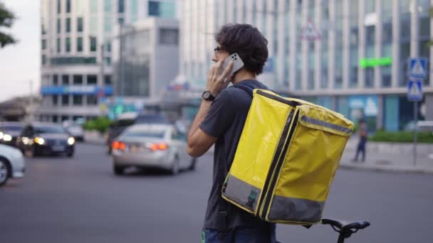 Доставщик с рюкзаком звонит клиенту на городской улице, вид сзади — стоковое видео
