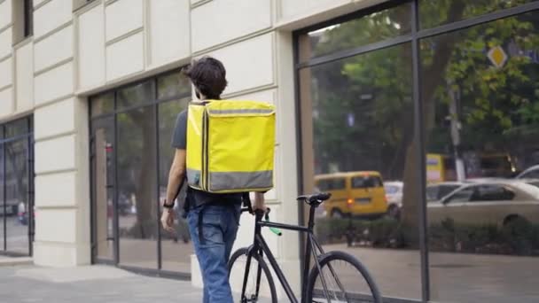 配達人は自転車と黄色のバッグで歩き、住所、リアビューを探しています — ストック動画