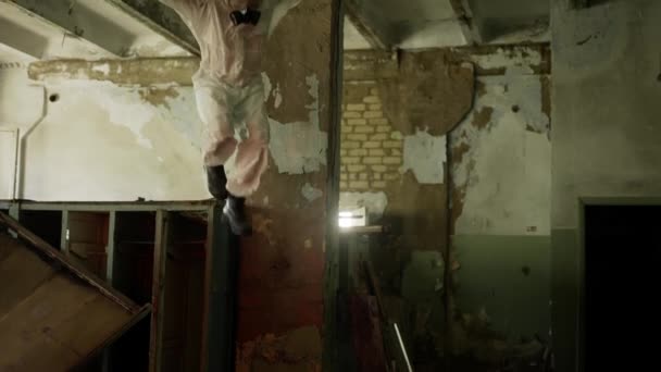Werknemer in beschermend pak in het geruïneerde gebouw springt uit de vernielde locker — Stockvideo